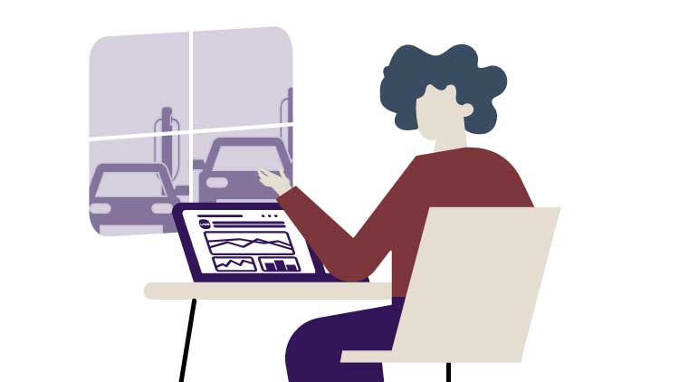 Person am Laptop sitzt vor einem Fenster durch das man ladende Autos sieht